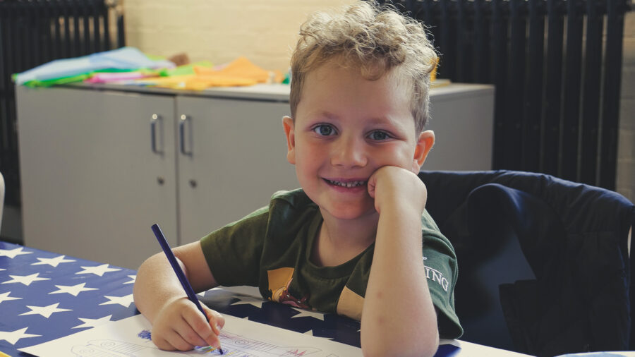 A young boy smiles at at the camera with a pencil in his hand, enjoying the family activities at Bletchley Park